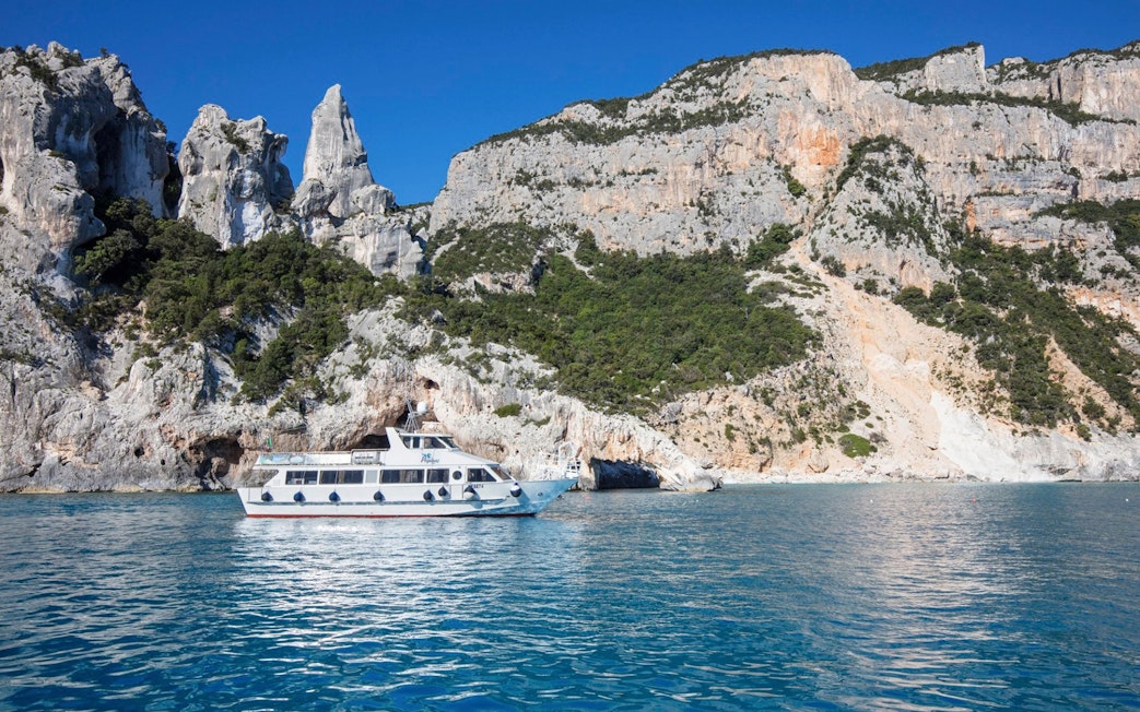 Boat cruising near rocky cliffs at Cala Minola, Gulf of Orosei, Italy.