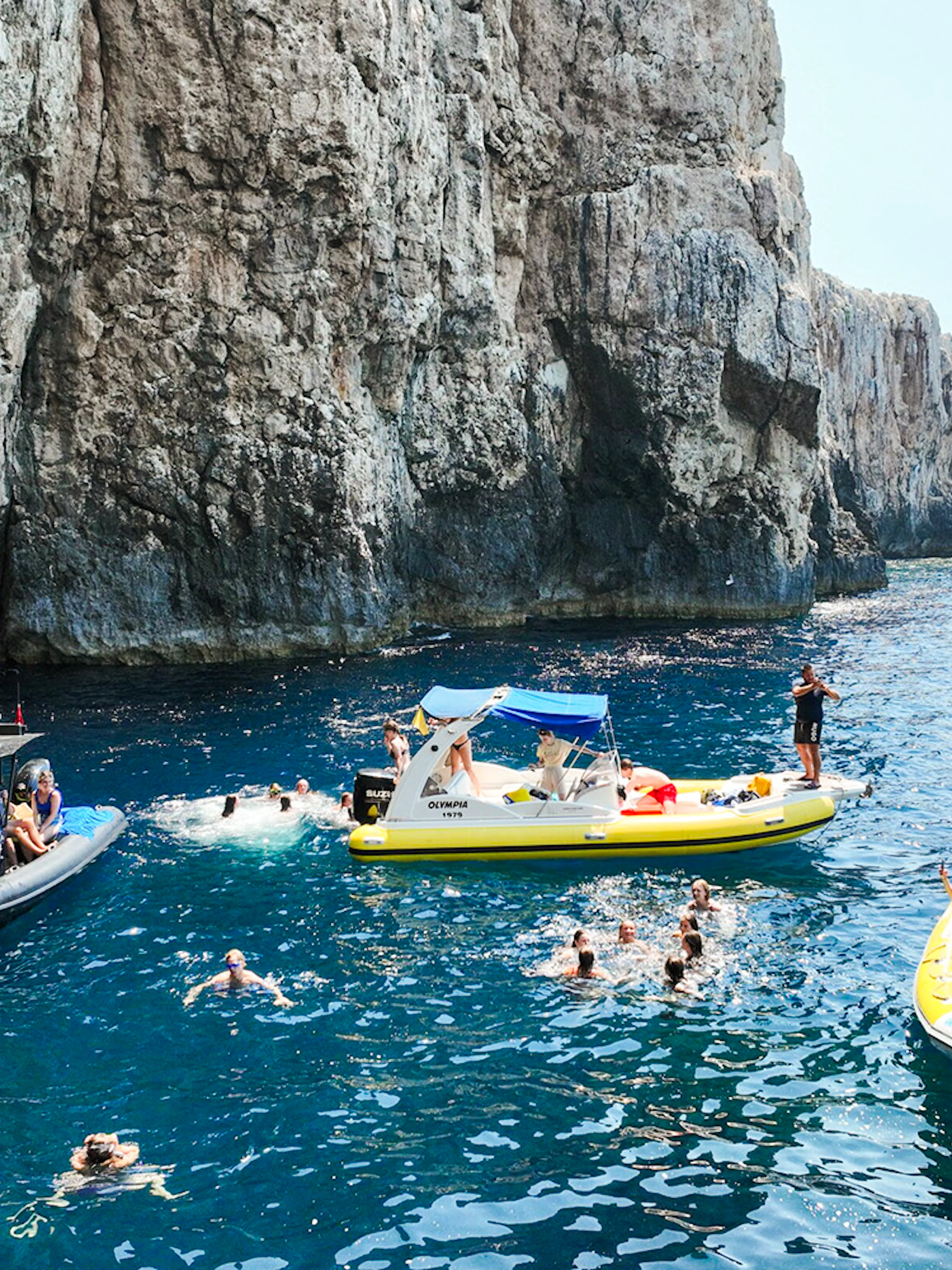 Small boats and swimmers near rocky cliffs at Dafina Bay and Haxhi Ali Cave.