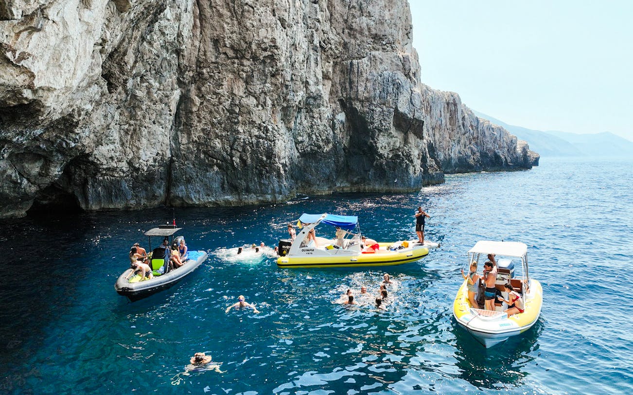 Small boats and swimmers near rocky cliffs at Dafina Bay and Haxhi Ali Cave.