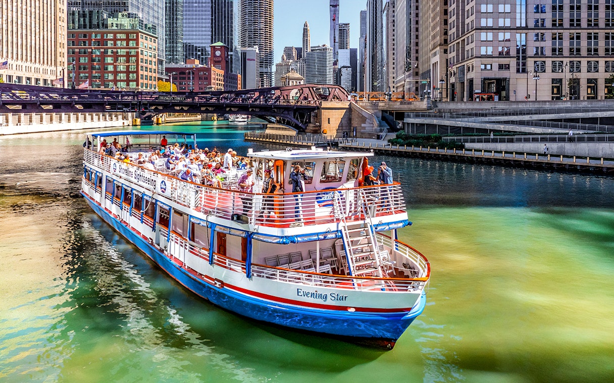 Tour boat on Chicago River with city skyline and bridge in background.