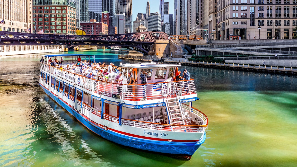 Tour boat on Chicago River with city skyline and bridge in background.
