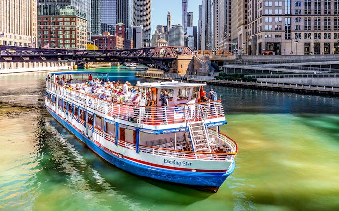 Tour boat on Chicago River with city skyline and bridge in background.