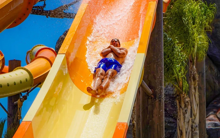 Person sliding down a water slide at Aqualand Torremolinos, surrounded by palm trees.