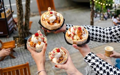 Hands holding bowls of ice cream with toppings during Da Nang local food tour.