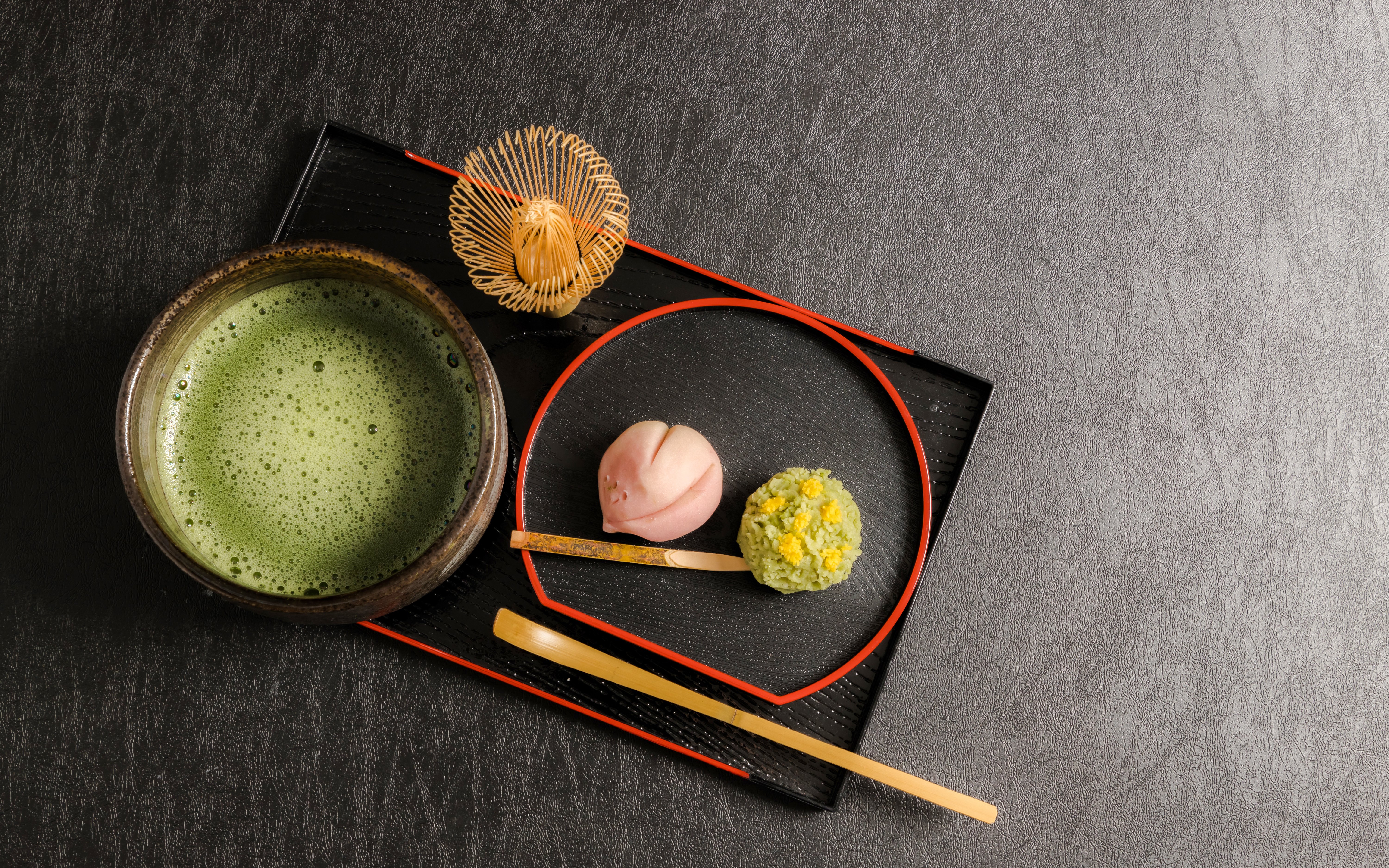 Wagashi sweets with a bowl of matcha tea on a black tray.
