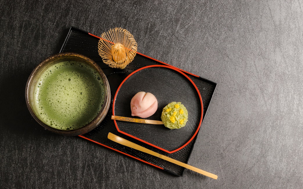 Wagashi sweets with a bowl of matcha tea on a black tray.