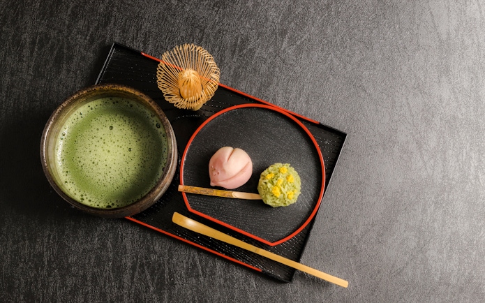 Wagashi sweets with a bowl of matcha tea on a black tray.