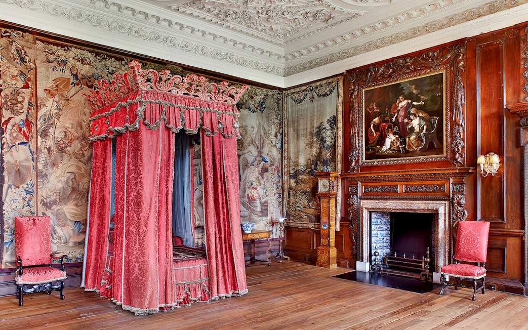 Ornate bedroom with red canopy bed and tapestries at Palace of Holyroodhouse, Edinburgh.