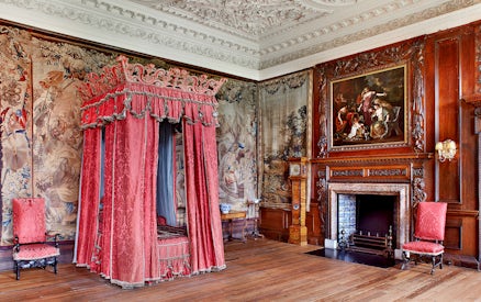 Ornate bedroom with red canopy bed and tapestries at Palace of Holyroodhouse, Edinburgh.