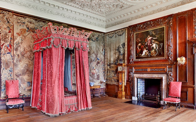 Ornate bedroom with red canopy bed and tapestries at Palace of Holyroodhouse, Edinburgh.