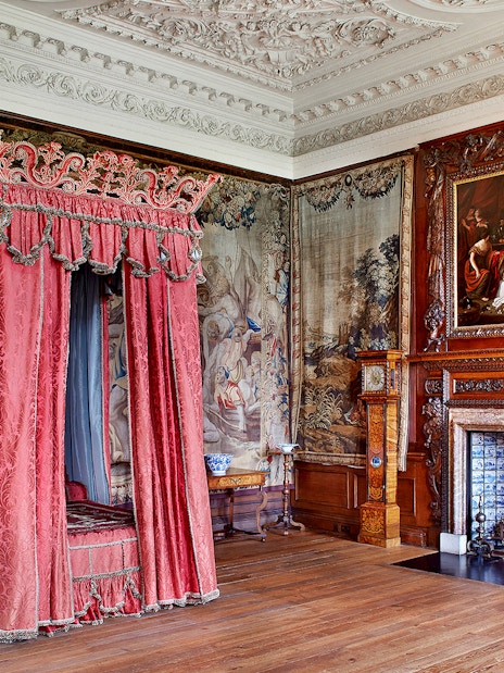 Ornate bedroom with red canopy bed and tapestries at Palace of Holyroodhouse, Edinburgh.