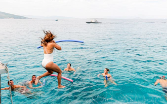 Group swimming in the Saronic Gulf, Greece, with a woman jumping from a boat.