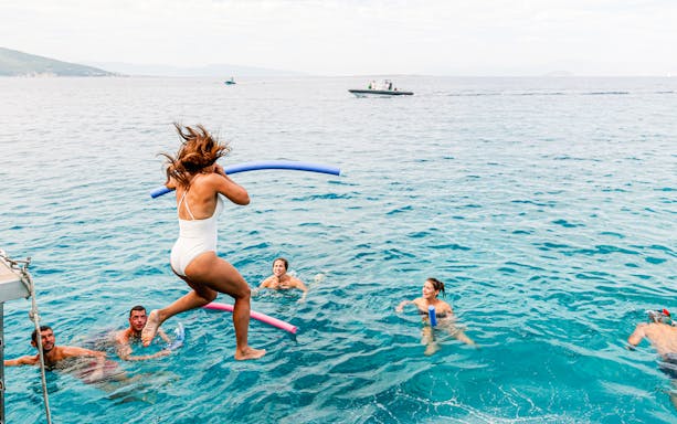 Group swimming in the Saronic Gulf, Greece, with a woman jumping from a boat.