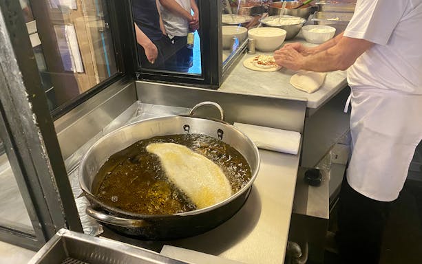Chef preparing fried pizza dough in a Naples street food kitchen.