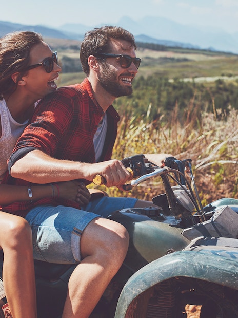 Couple riding an ATV during a quad safari in Antalya, with scenic landscape in the background.