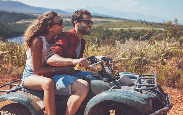 Couple riding an ATV during a quad safari in Antalya, with scenic landscape in the background.