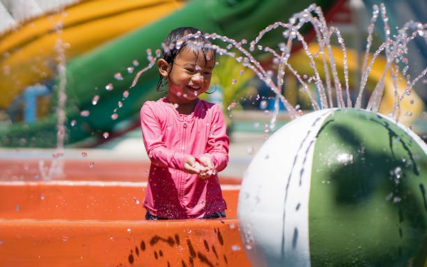 Child enjoying water fountains at a colorful waterpark.