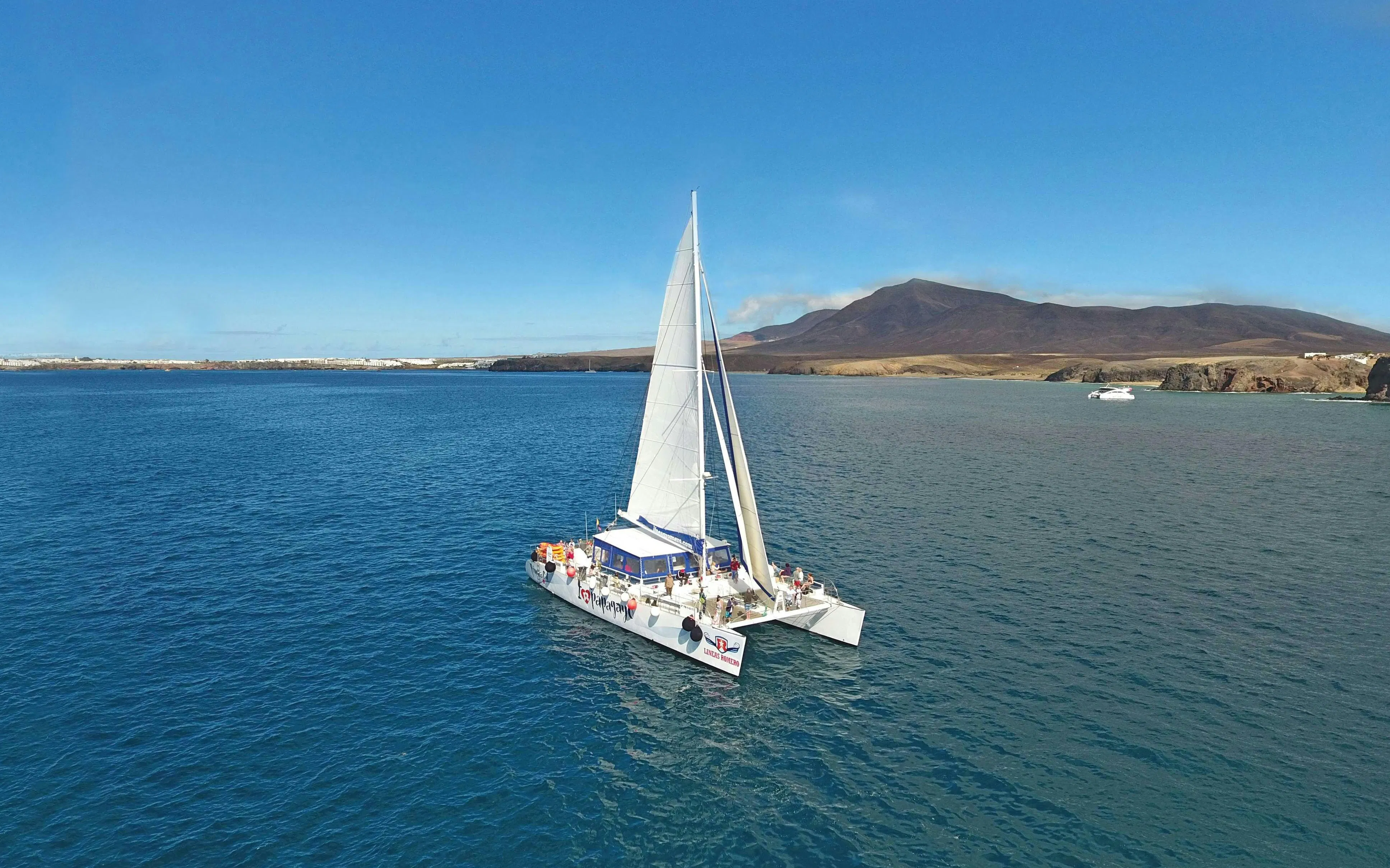 Catamaran sailing near Papagayo Beaches, Lanzarote, with distant mountains in view.