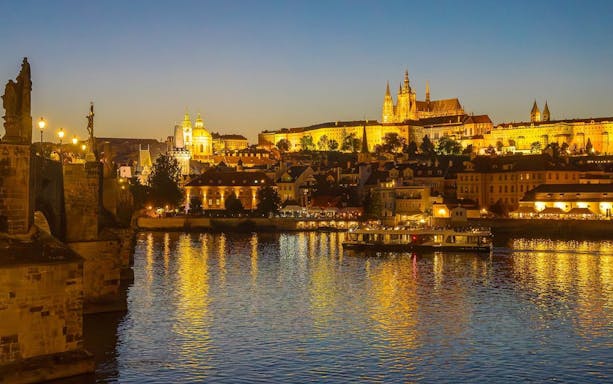 Evening cruise on Vltava River with view of Prague Castle and Charles Bridge.