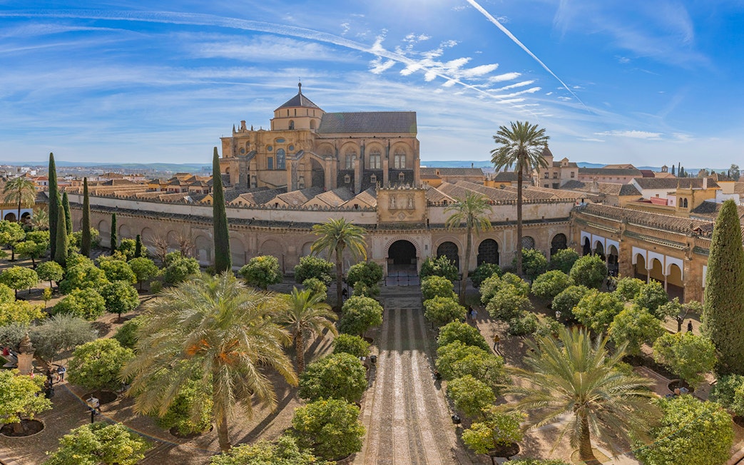 Cordoba Mosque-Cathedral exterior with gardens and palm trees under a blue sky.