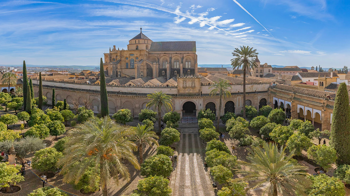 Cordoba Mosque-Cathedral exterior with gardens and palm trees under a blue sky.