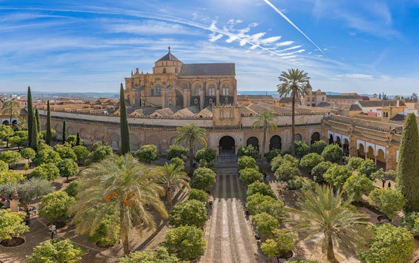 Cordoba Mosque-Cathedral exterior with gardens and palm trees under a blue sky.