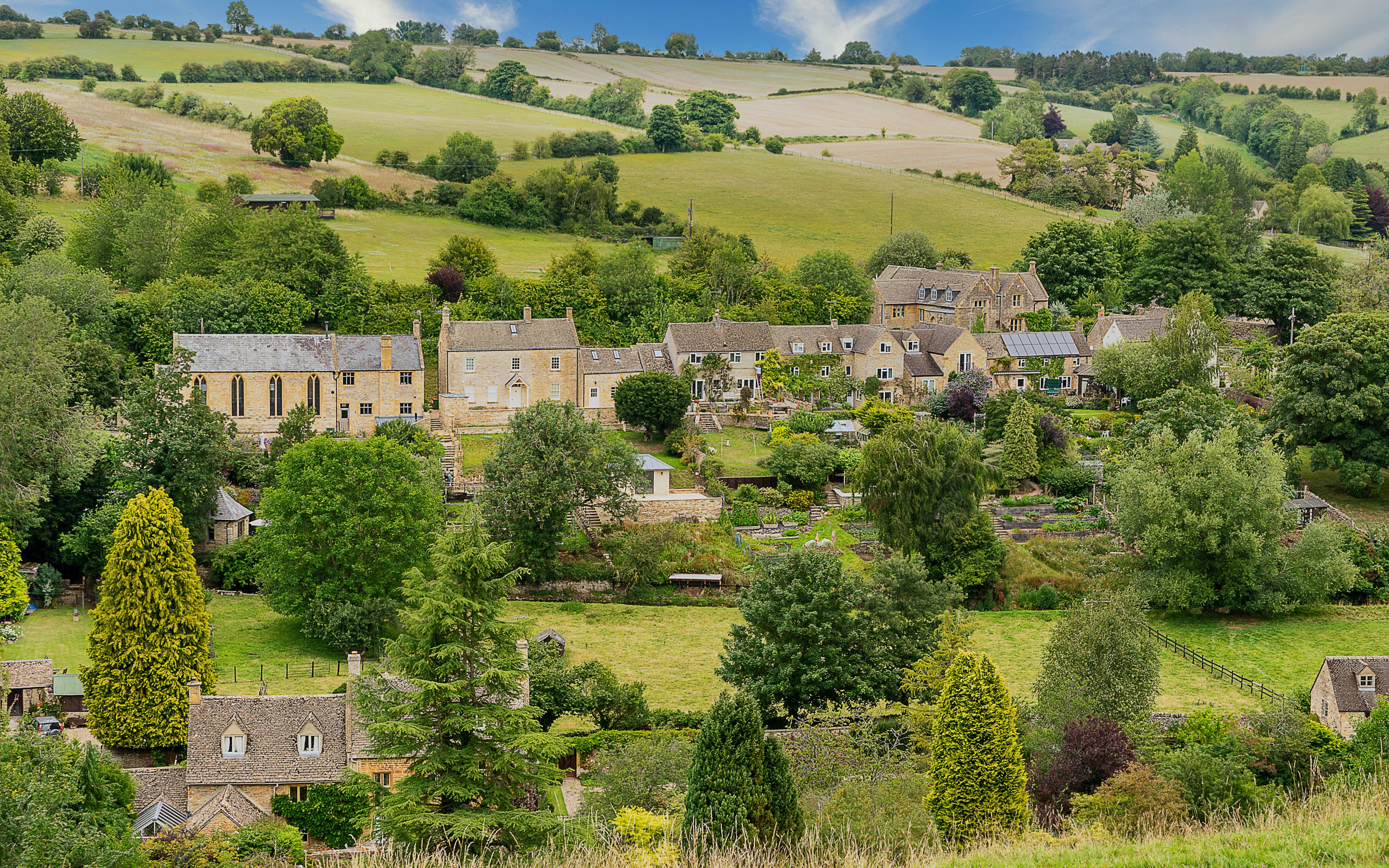 Cotswold village with stone cottages and lush green landscape.
