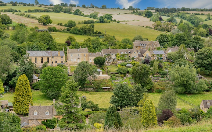 Cotswold village with stone cottages and lush green landscape.