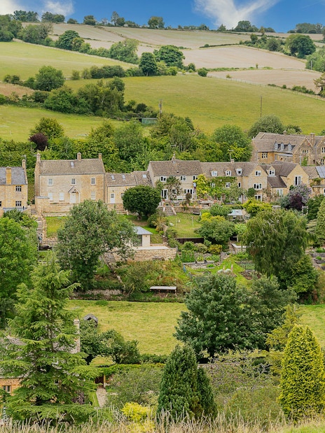 Cotswold village with stone cottages and lush green landscape.