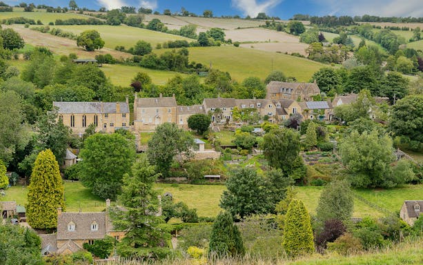 Cotswold village with stone cottages and lush green landscape.