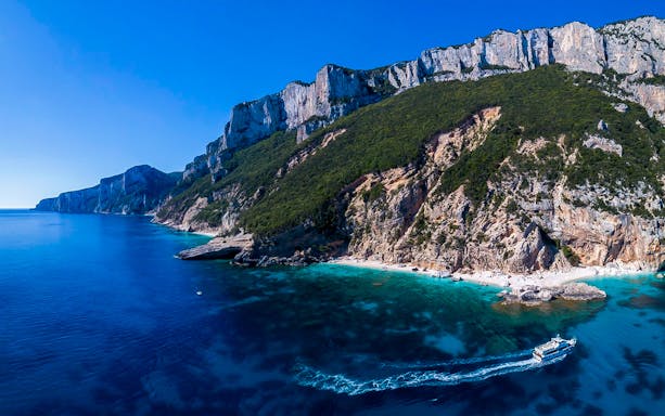 Cruise boat near cliffs and turquoise waters in Gulf of Orosei, Sardinia.