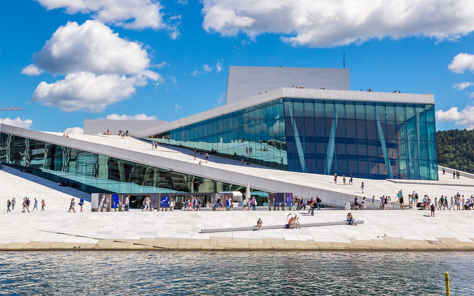 Oslo Opera House with visitors walking on its sloped roof by the waterfront.