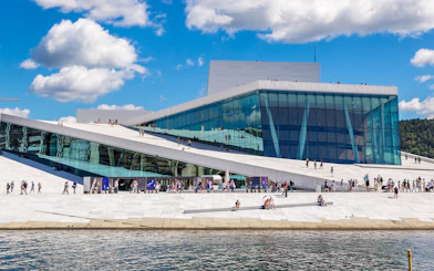 Oslo Opera House with visitors walking on its sloped roof by the waterfront.