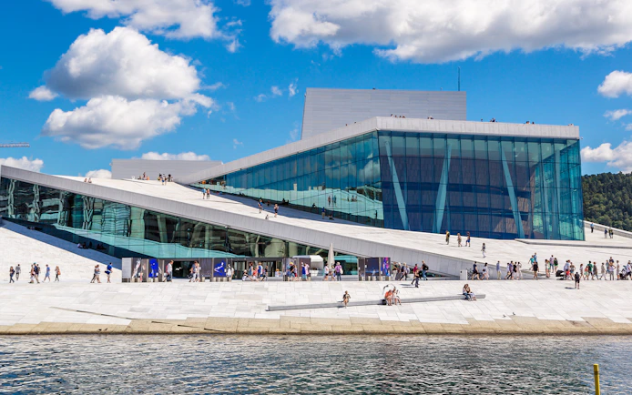 Oslo Opera House with visitors walking on its sloped roof by the waterfront.