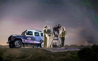 Stargazing at Mleiha Sunset Lounge with telescope and off-road vehicle in desert.