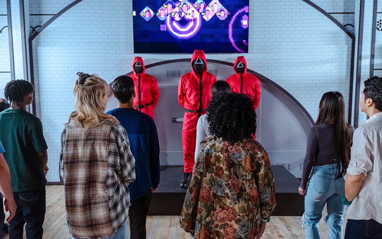 Visitors facing masked guards in red suits at Squid Games experience, London.