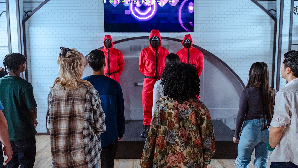 Visitors facing masked guards in red suits at Squid Games experience, London.