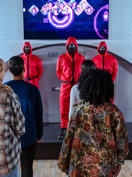 Visitors facing masked guards in red suits at Squid Games experience, London.