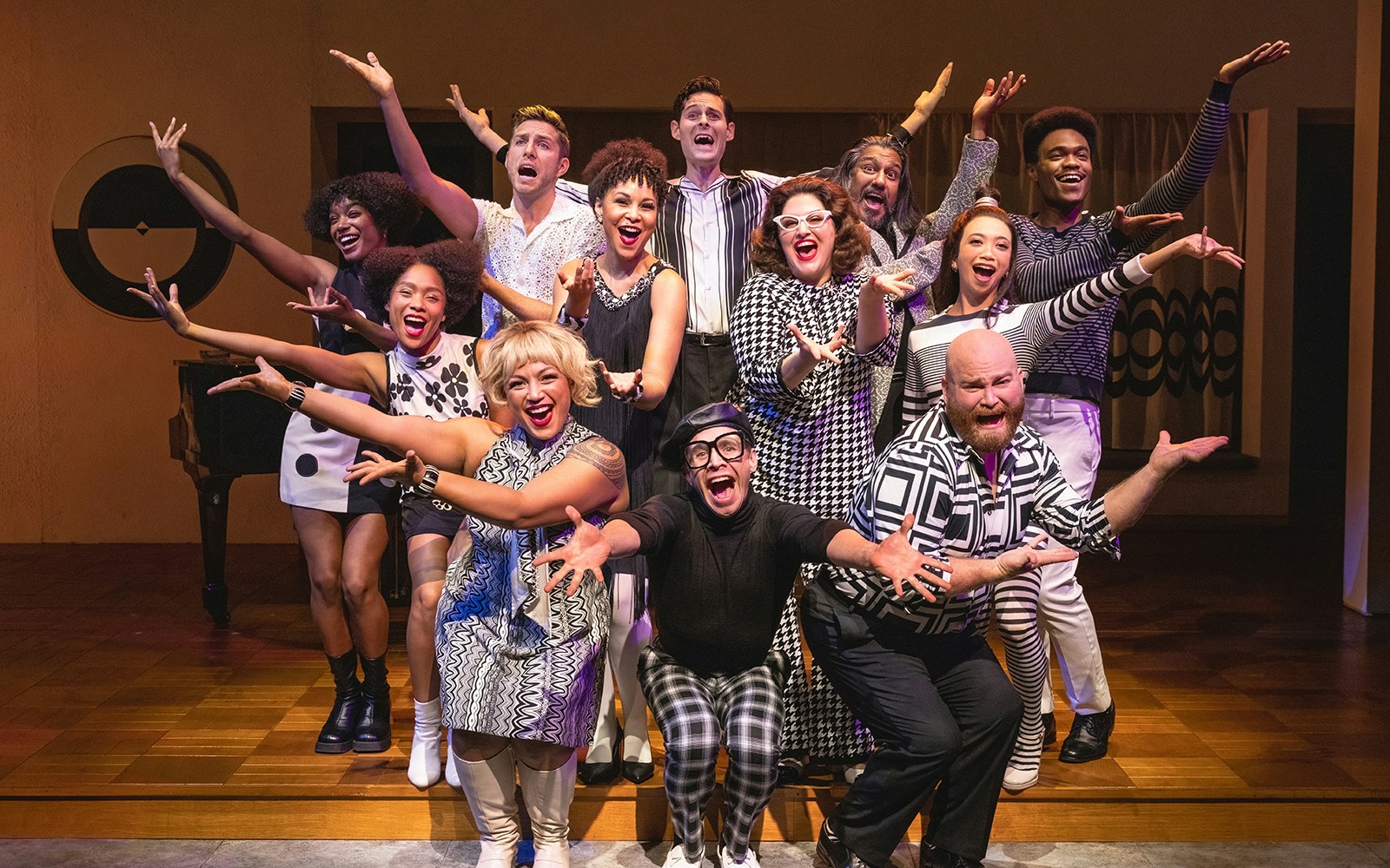 Cast of "Merrily We Roll Along" performing on stage, arms outstretched in a lively pose.