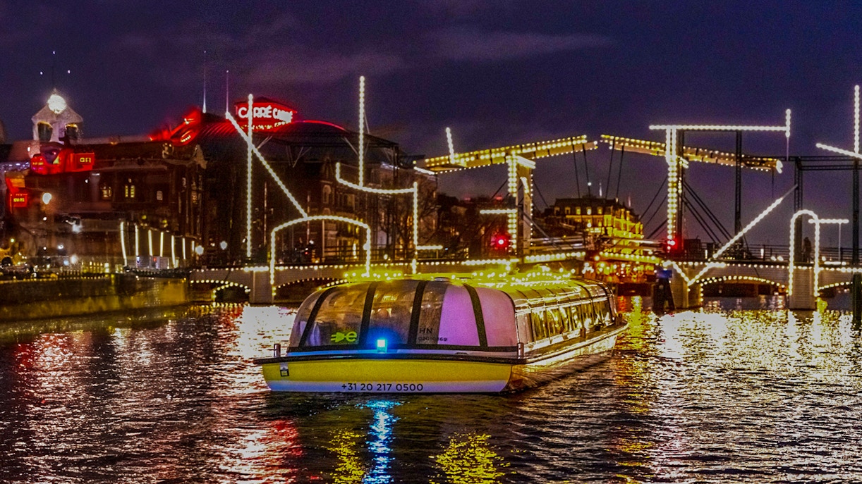Canal boat cruising under illuminated bridges during Amsterdam Lights Festival.