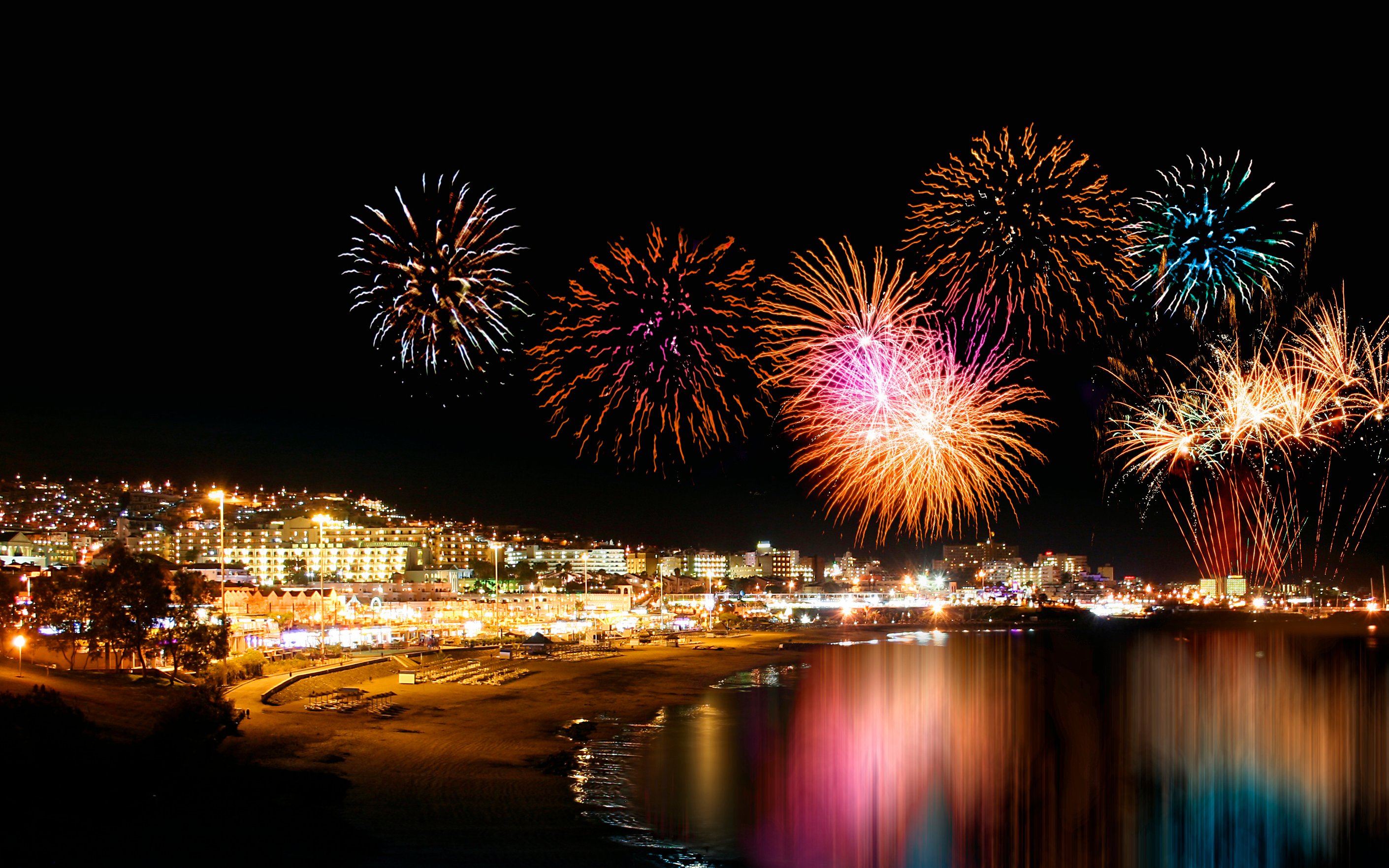 Fireworks display over a lit-up coastal city in Tenerife at night.
