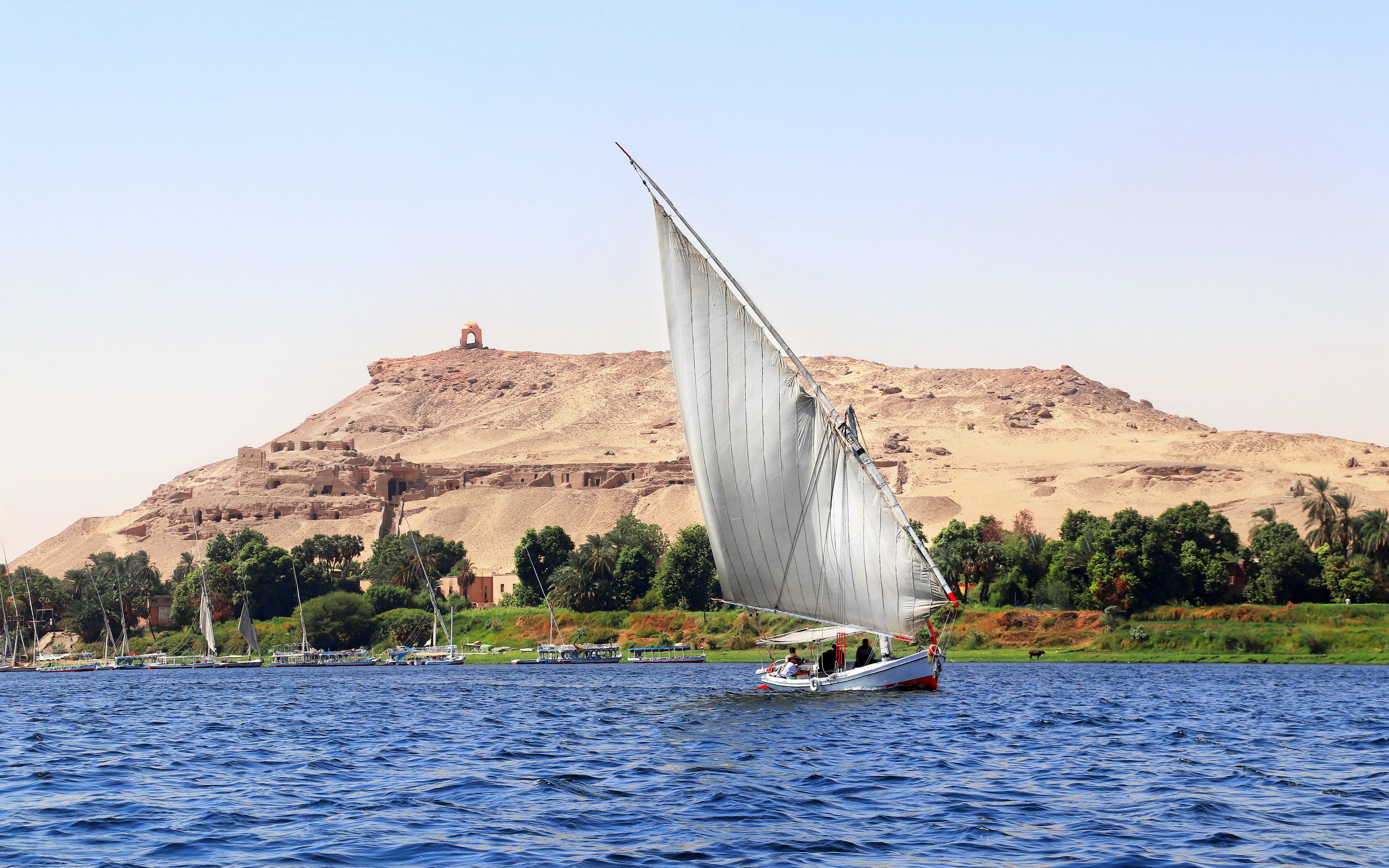 Felucca sailing on the Nile River with desert hills in Cairo.