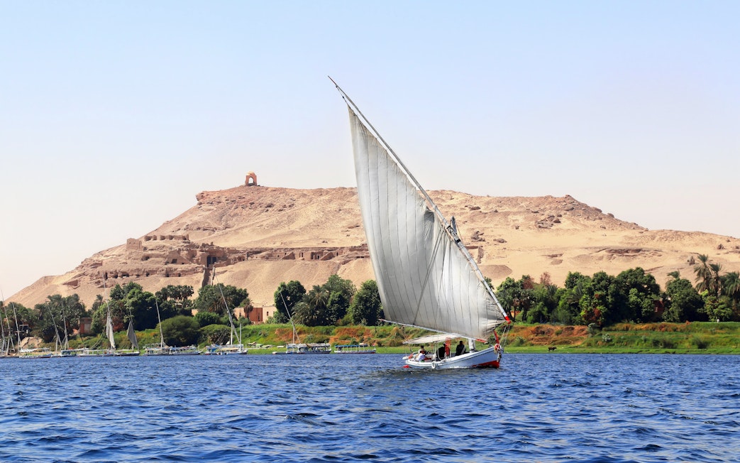 Felucca sailing on the Nile River with desert hills in Cairo.