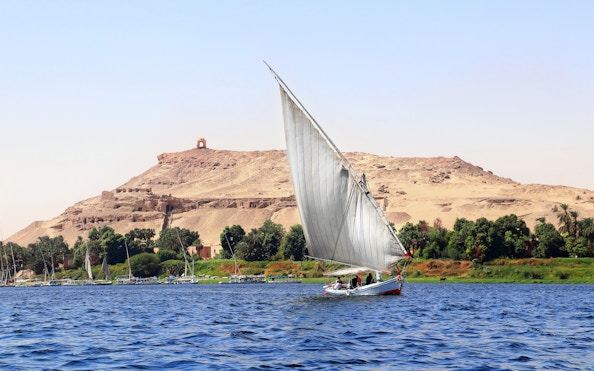 Felucca sailing on the Nile River with desert hills in Cairo.