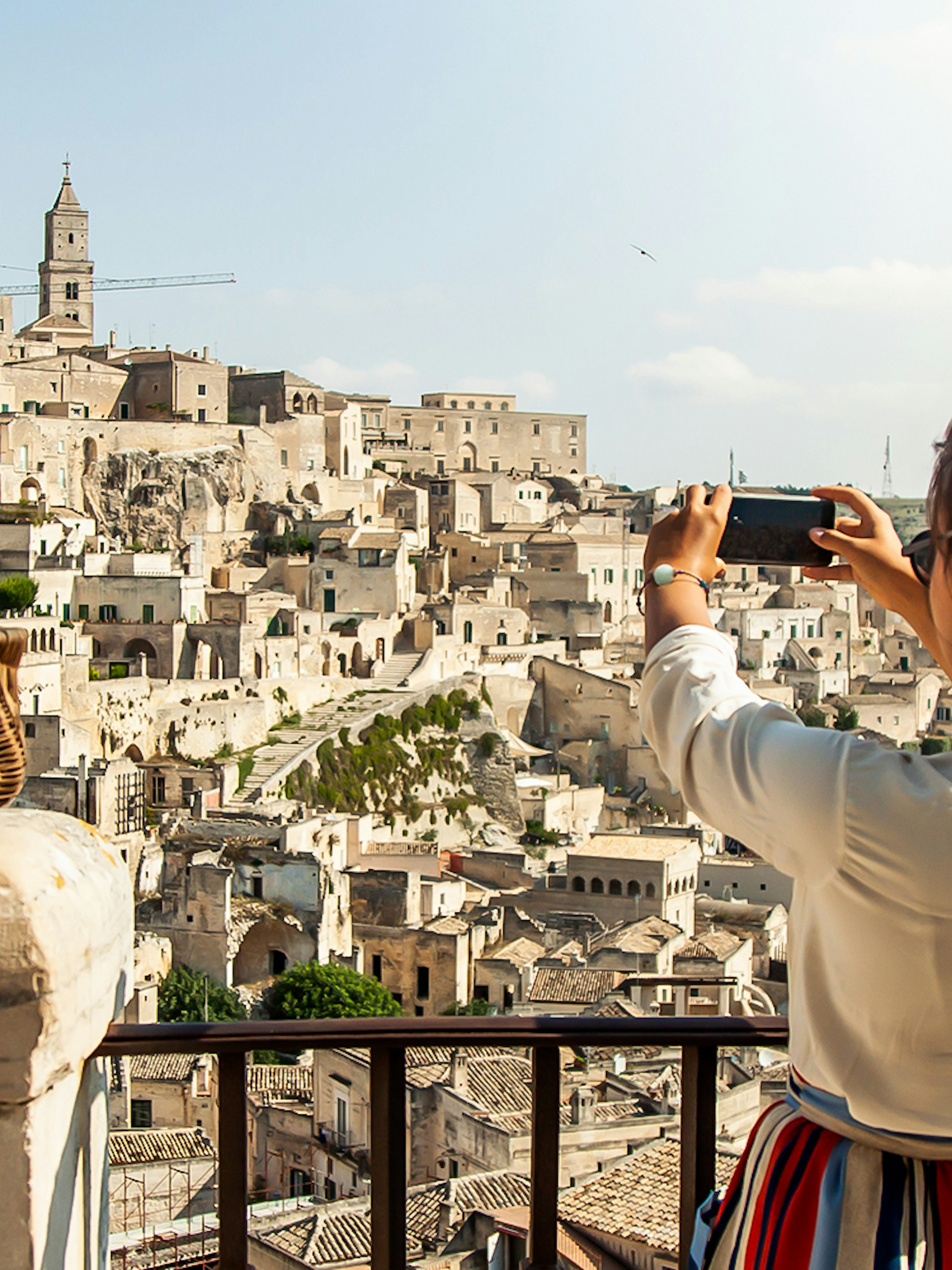 Person photographing Sassi of Matera with a basket of flowers in the foreground.