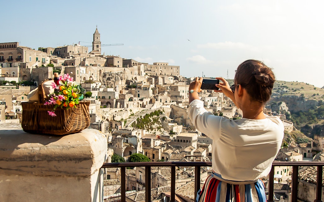 Person photographing Sassi of Matera with a basket of flowers in the foreground.