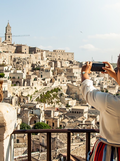 Person photographing Sassi of Matera with a basket of flowers in the foreground.