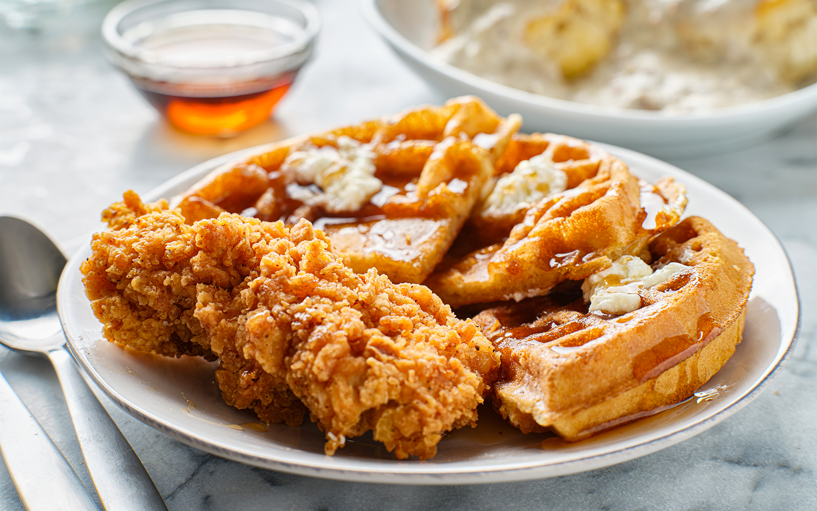 Chicken and waffles breakfast served on a white plate with syrup on the side.