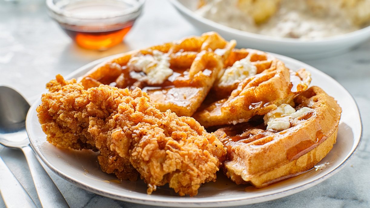 Crispy fried chicken with waffles and syrup on a plate.