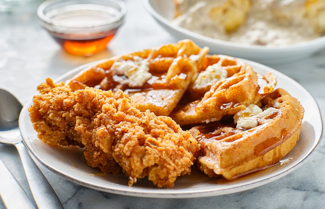 Chicken and waffles breakfast served on a white plate with syrup on the side.